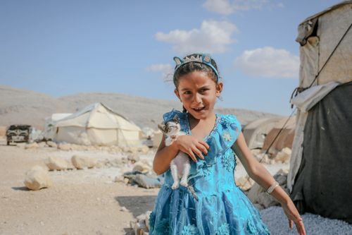 Free A child joyfully holds a kitten in a Syrian refugee camp, showcasing resilience and hope. Stock Photo