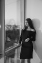 Young woman in formal dress standing and looking through office window
