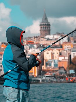 Man fishing by the iconic Galata Tower in Istanbul, capturing leisure and urban scenery.