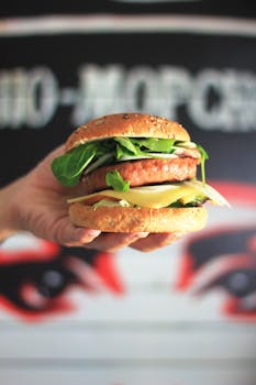 Close-up of a gourmet burger with arugula and cheese being held, perfect for foodie stock images.