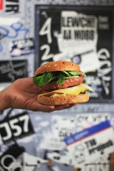 A delicious gourmet vegan burger with fresh greens held against a graffiti-covered wall.