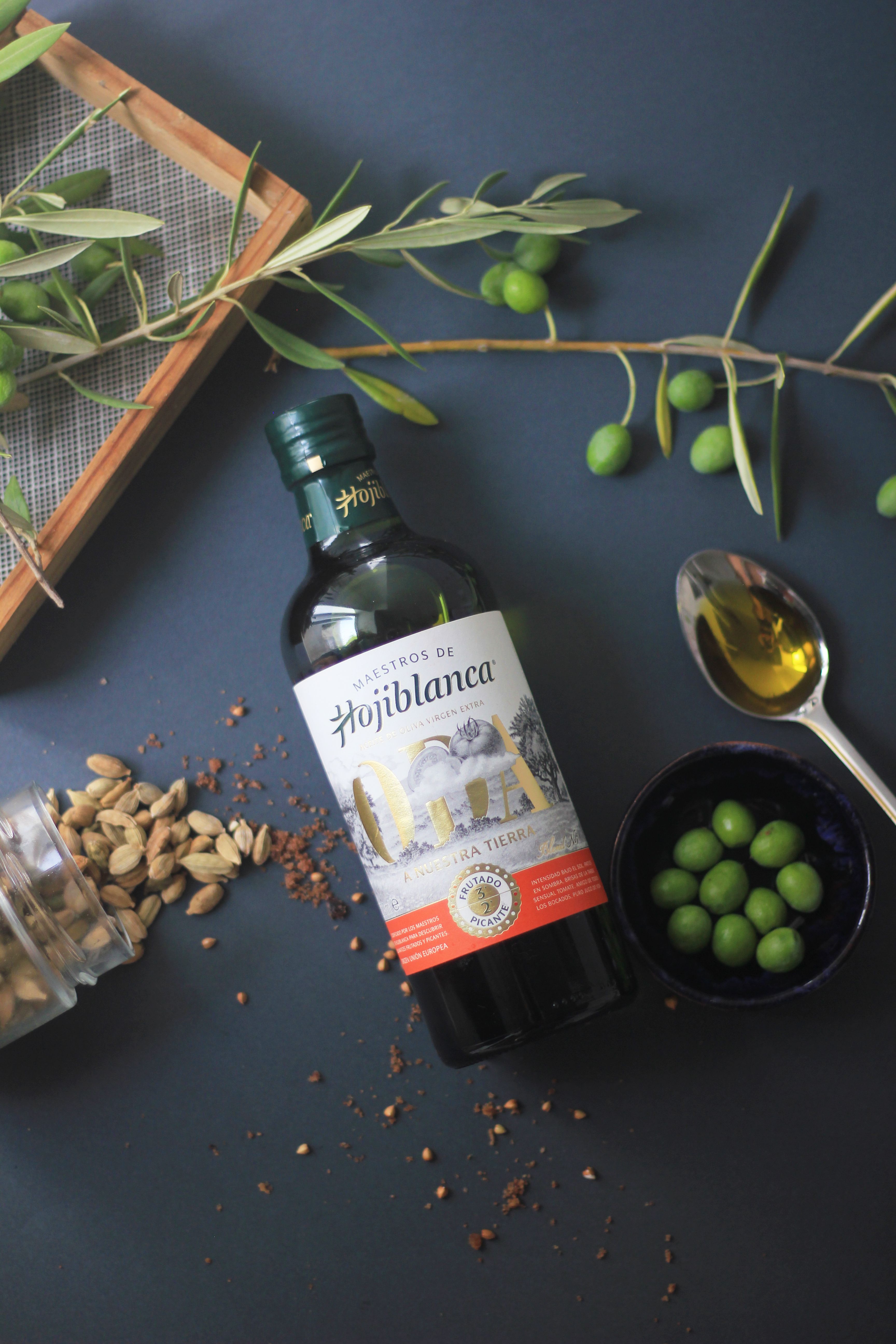 Top view of Hojiblanca olive oil bottle with fresh olives and spices for culinary use.