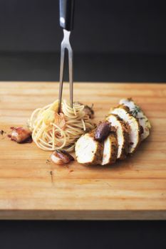 Sliced chicken breast with garlic-infused spaghetti on a wooden cutting board, presented with culinary elegance.