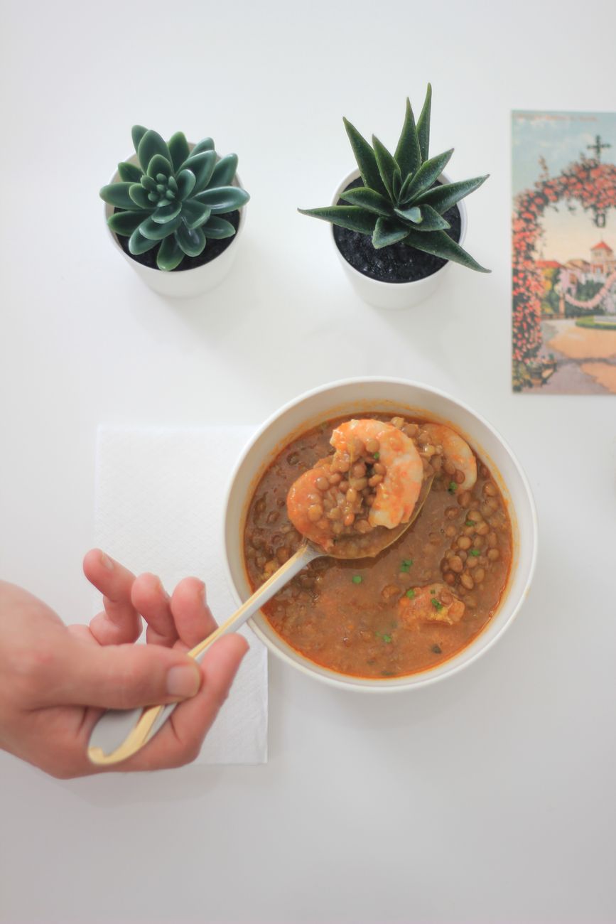 A bowl of thick, reddish-brown Ethiopian misir wot garnished with a sprig of herbs, served alongside pieces of injera bread