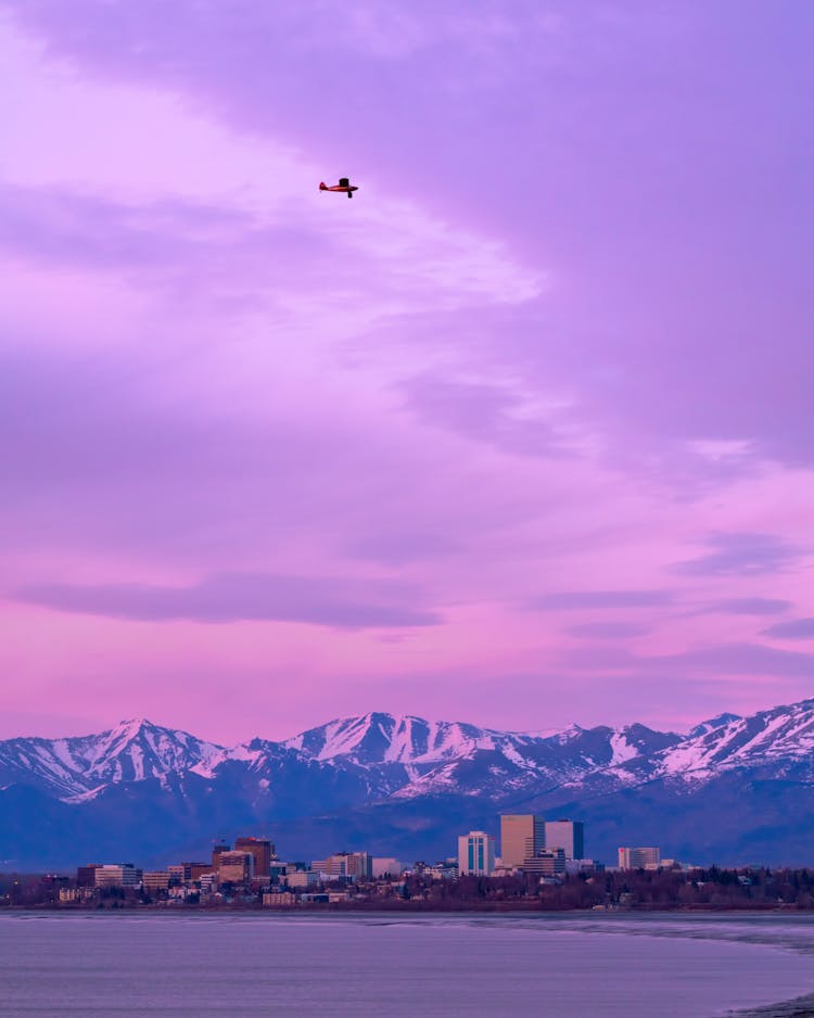 Plane Above Mountains In Snow On Pink Sunset