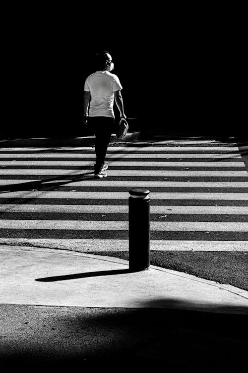 Monochrome Photo of a Pedestrian Crossing a Road