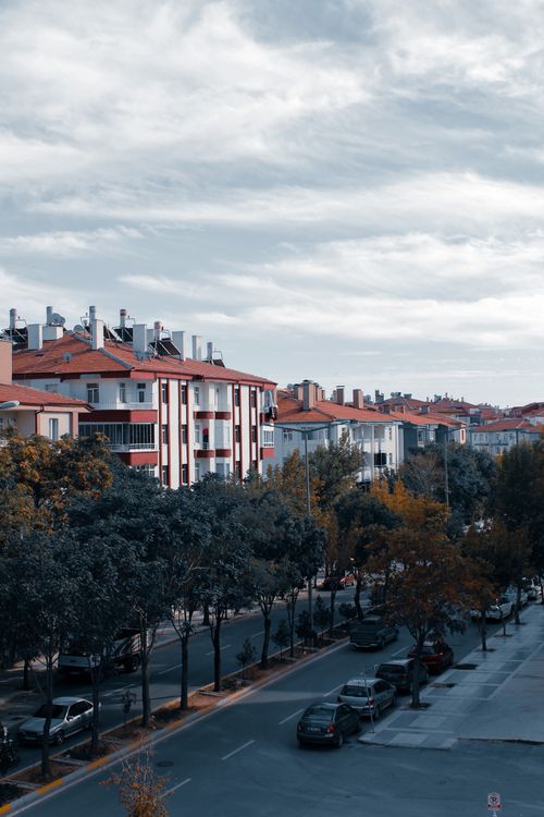 Free Aerial view of a modern city street lined with red roof buildings and trees on a cloudy day. Stock Photo