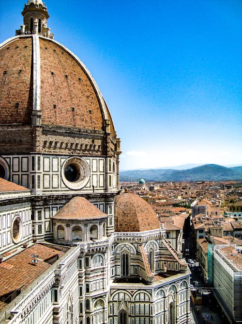 Brown and White Painted Cathedral Roof Overlooking City and Mountain Under Blue Sky