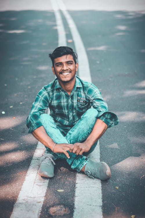 A Man in Plaid Button Up Shirt and Denim Jeans Sitting on the Road