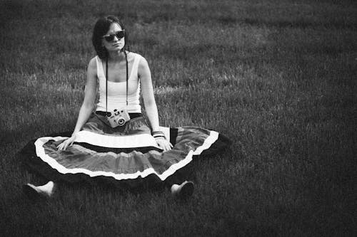 Free Woman in White Tank Top and Skirt Sitting on Grass Field in Grayscale Photography Stock Photo