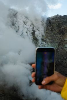 Close-up of a smartphone taking a photo of a steaming volcanic eruption, showcasing nature's power.