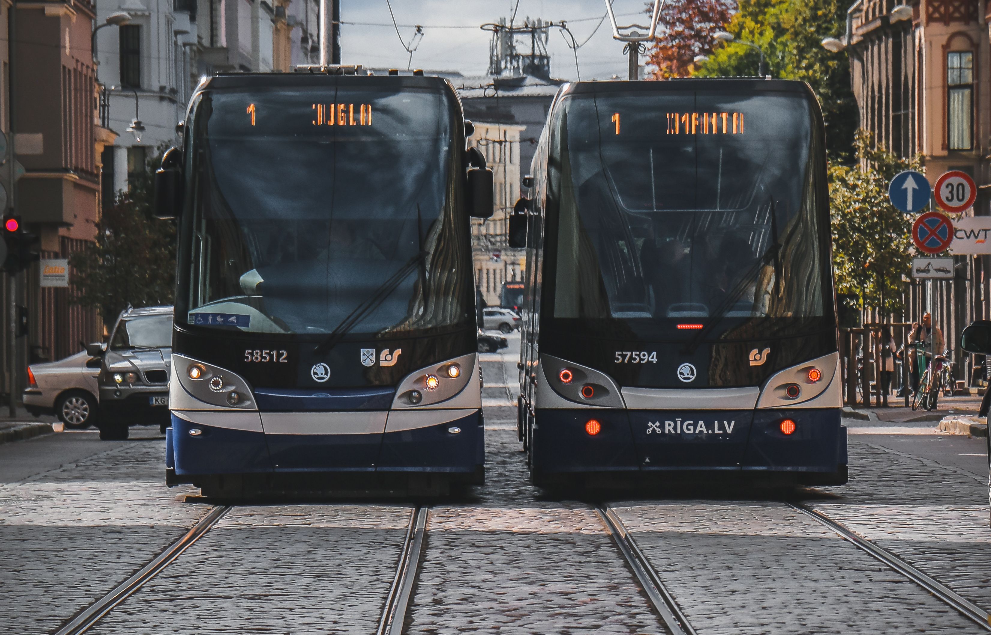 Two modern trams on cobblestone streets in Riga, Latvia, under a clear day sky.