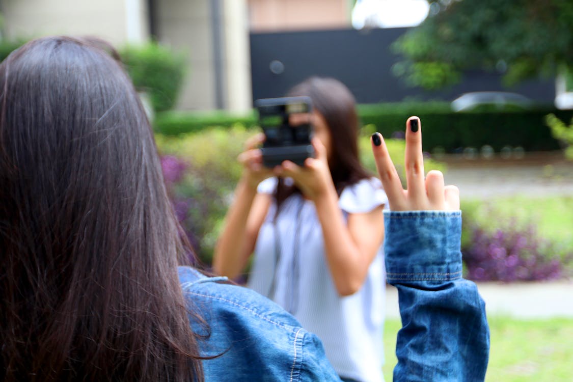 Woman Holding Camera While Taking Picture Of A Woman With A Peace Finger Sign