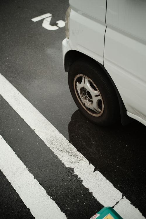 Free Close-up of a parked vehicle on a rainy asphalt road with visible white lines and markings. Stock Photo