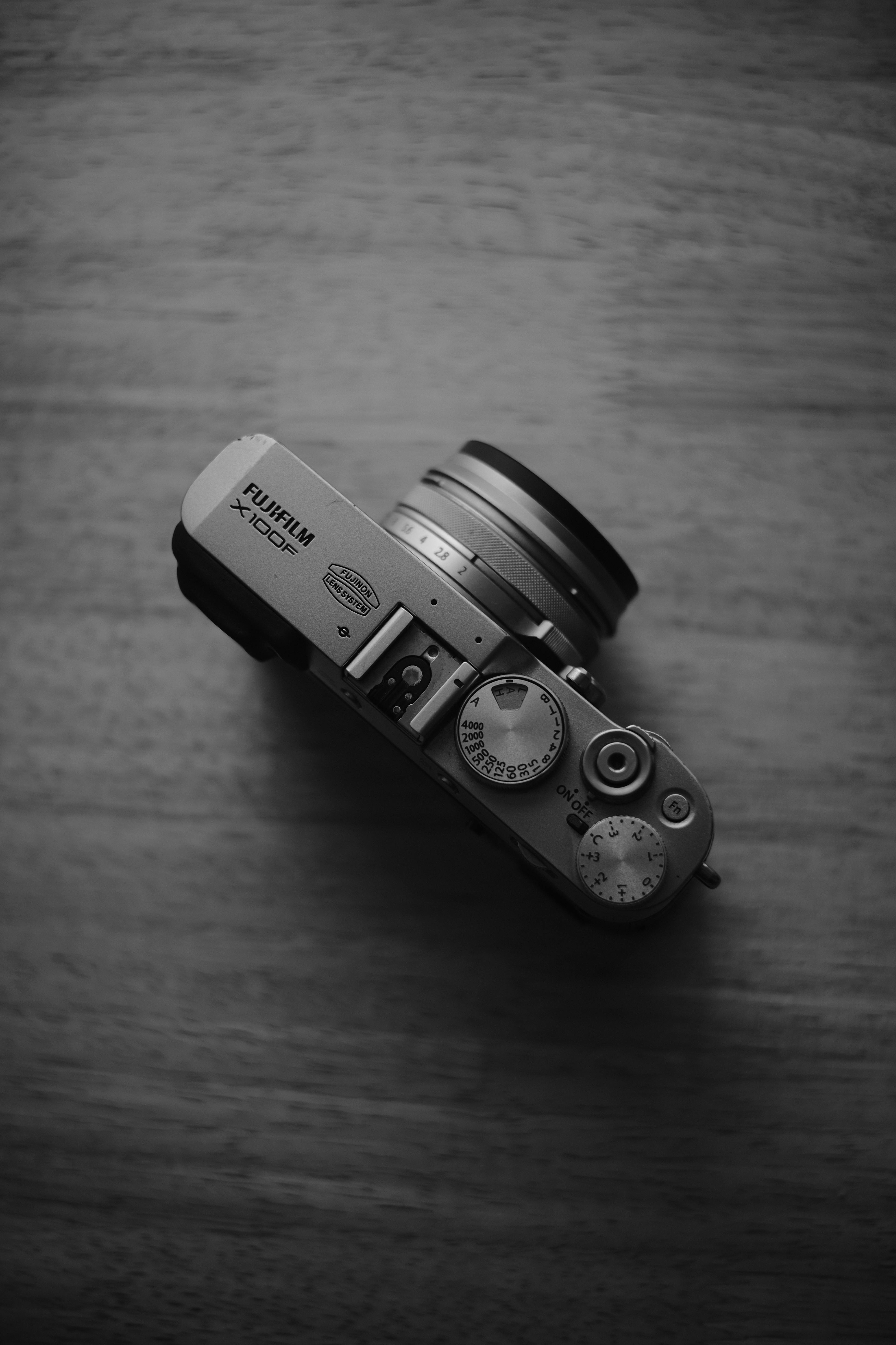 Black and white photo of a vintage-style digital camera from above on wooden table.