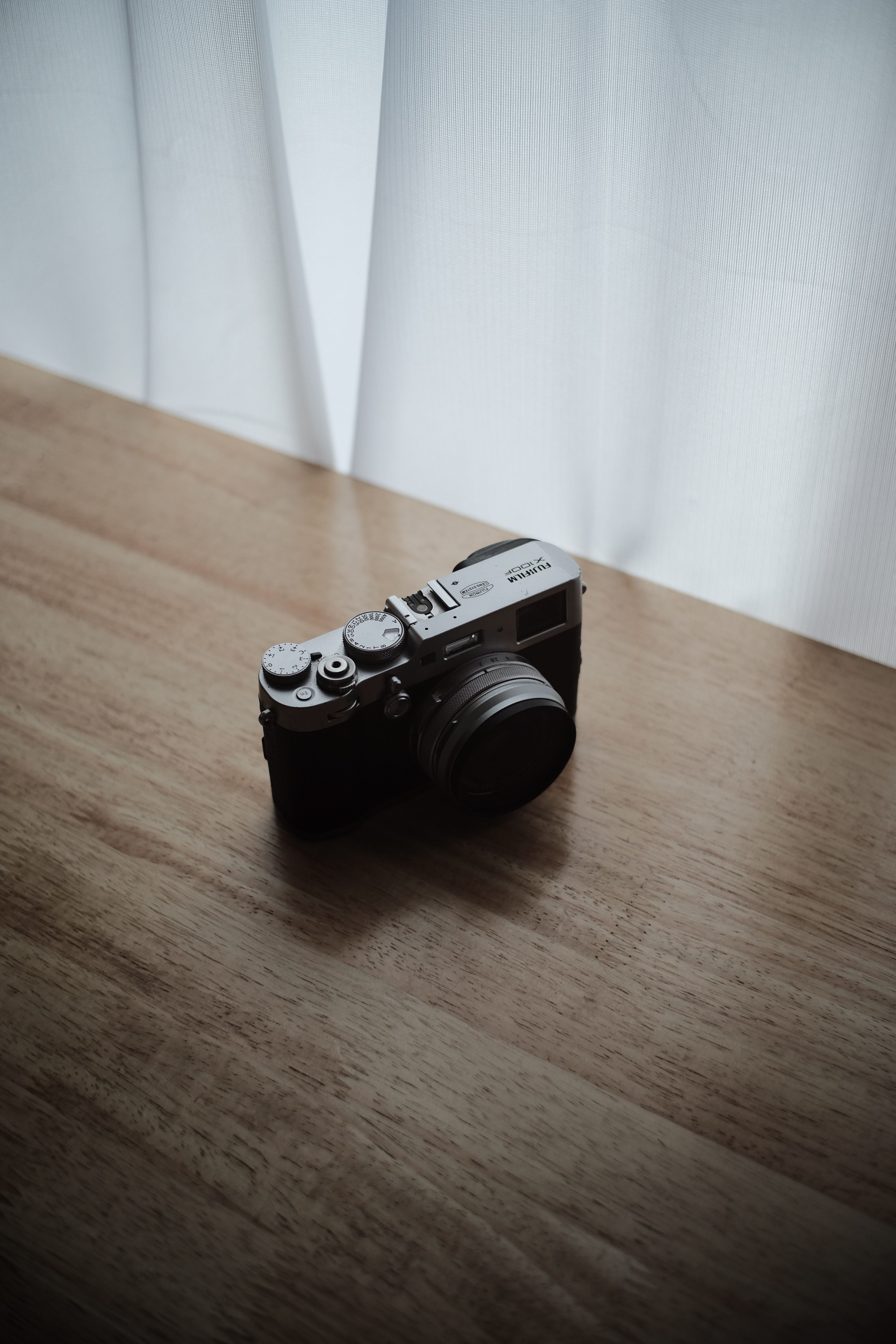 A compact digital camera resting on a wooden surface, captured in natural indoor lighting.
