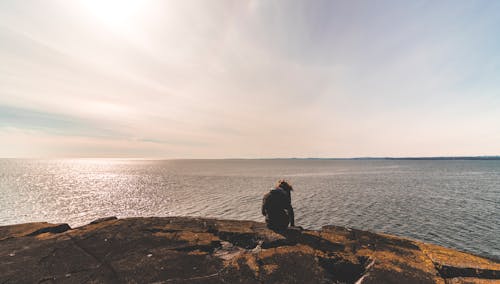 Free Person Sitting on Stone in Front of Sea Water Stock Photo