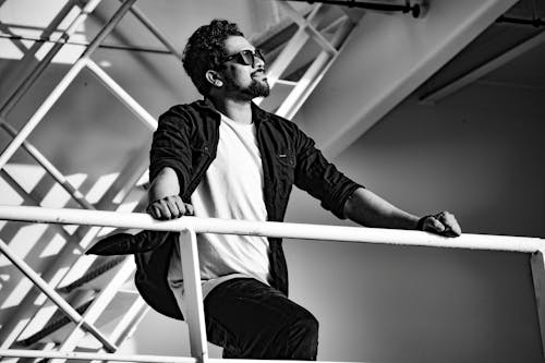 A Bearded Man in Black and White Top Standing Near Railing