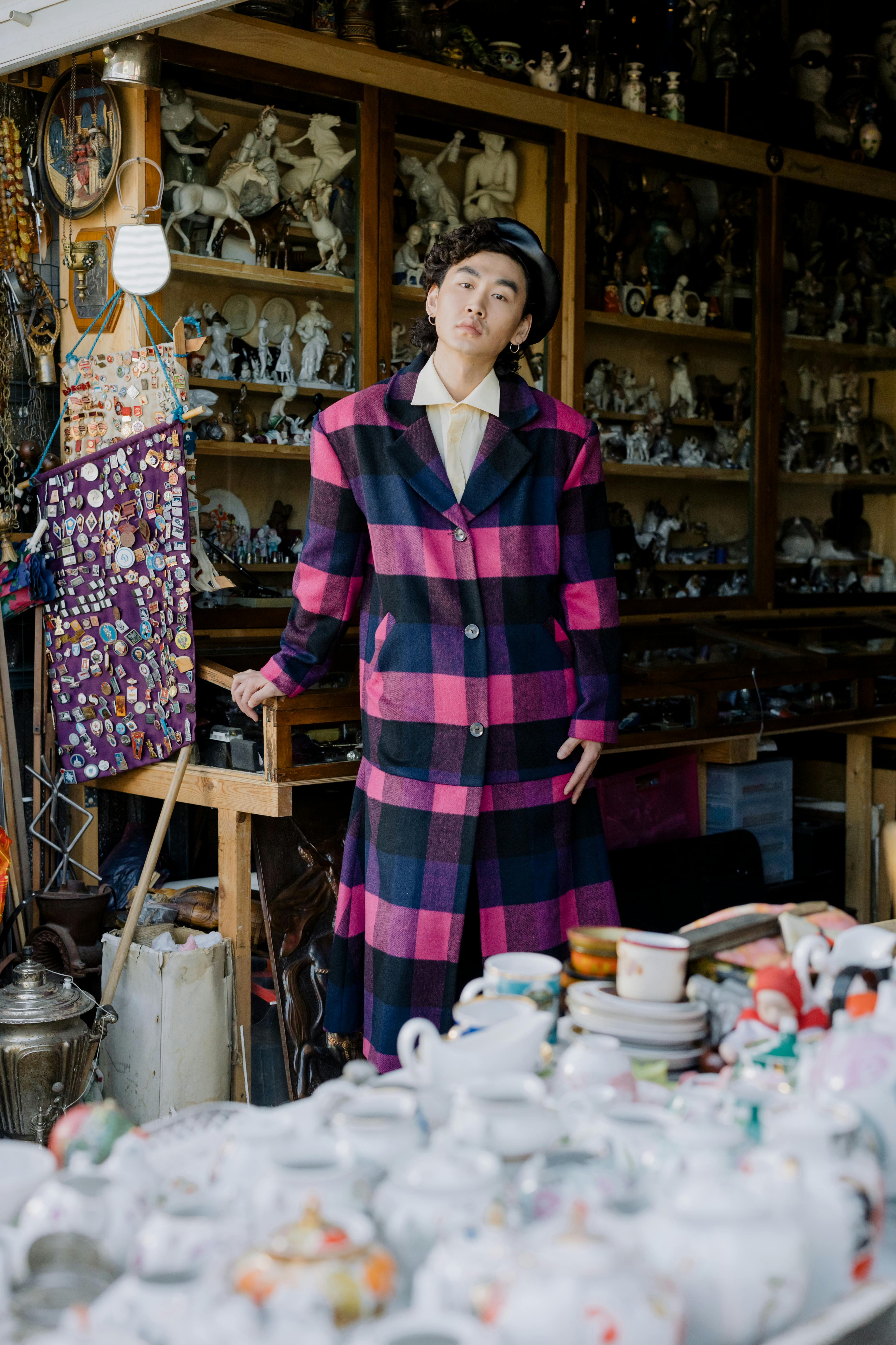 Fashionable man posing in a colorful checkered coat surrounded by vintage collectibles.