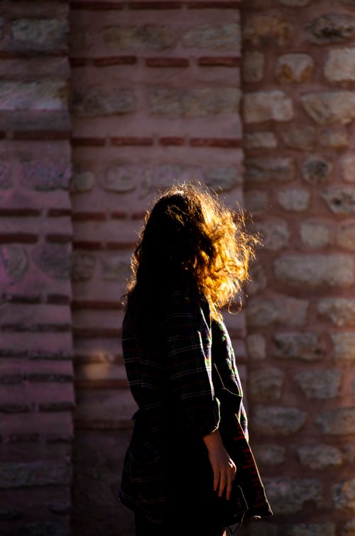Free A silhouette of a woman with curly hair captured against a textured stone wall in warm lighting. Stock Photo