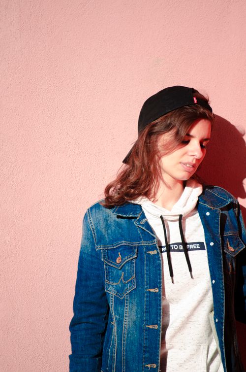 Free Young woman wearing denim jacket and cap against pink wall, exuding a stylish urban vibe. Stock Photo