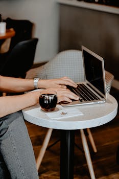 Adult male using laptop in a cozy coffee shop setting with a beverage nearby.