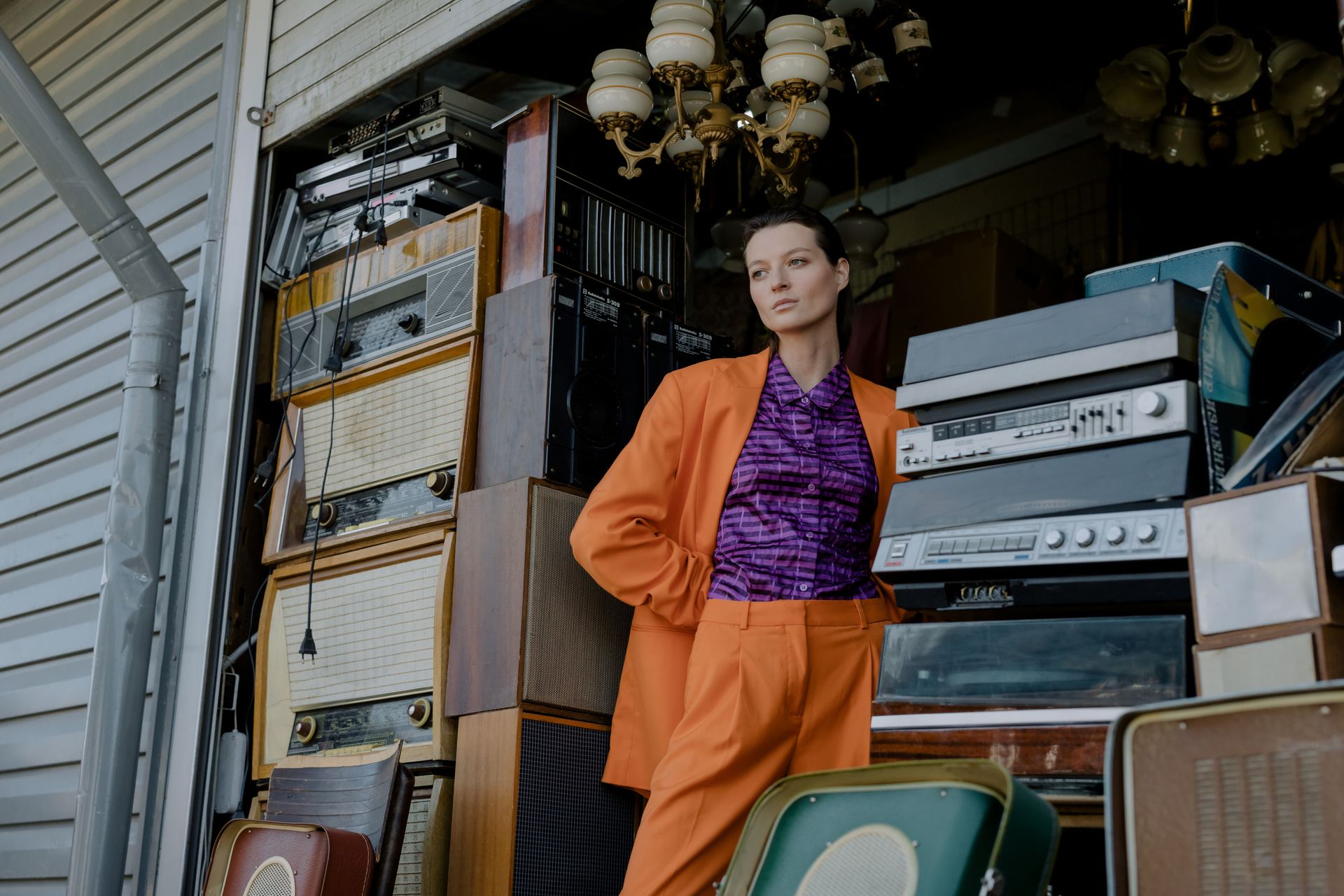 A Woman in Orange Blazer Standing Beside Vintage Radio
