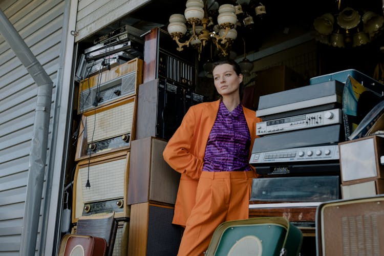 A Woman In Orange Blazer Standing Beside Vintage Radio