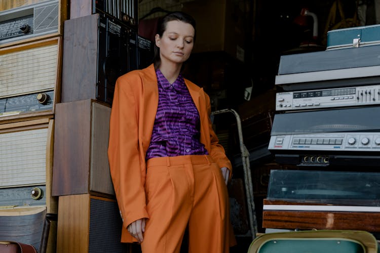 A Woman In Orange Suit Leaning On A Stack Of Speakers