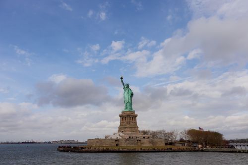 Free Iconic Statue of Liberty against a partly cloudy sky in New York Harbor. Stock Photo