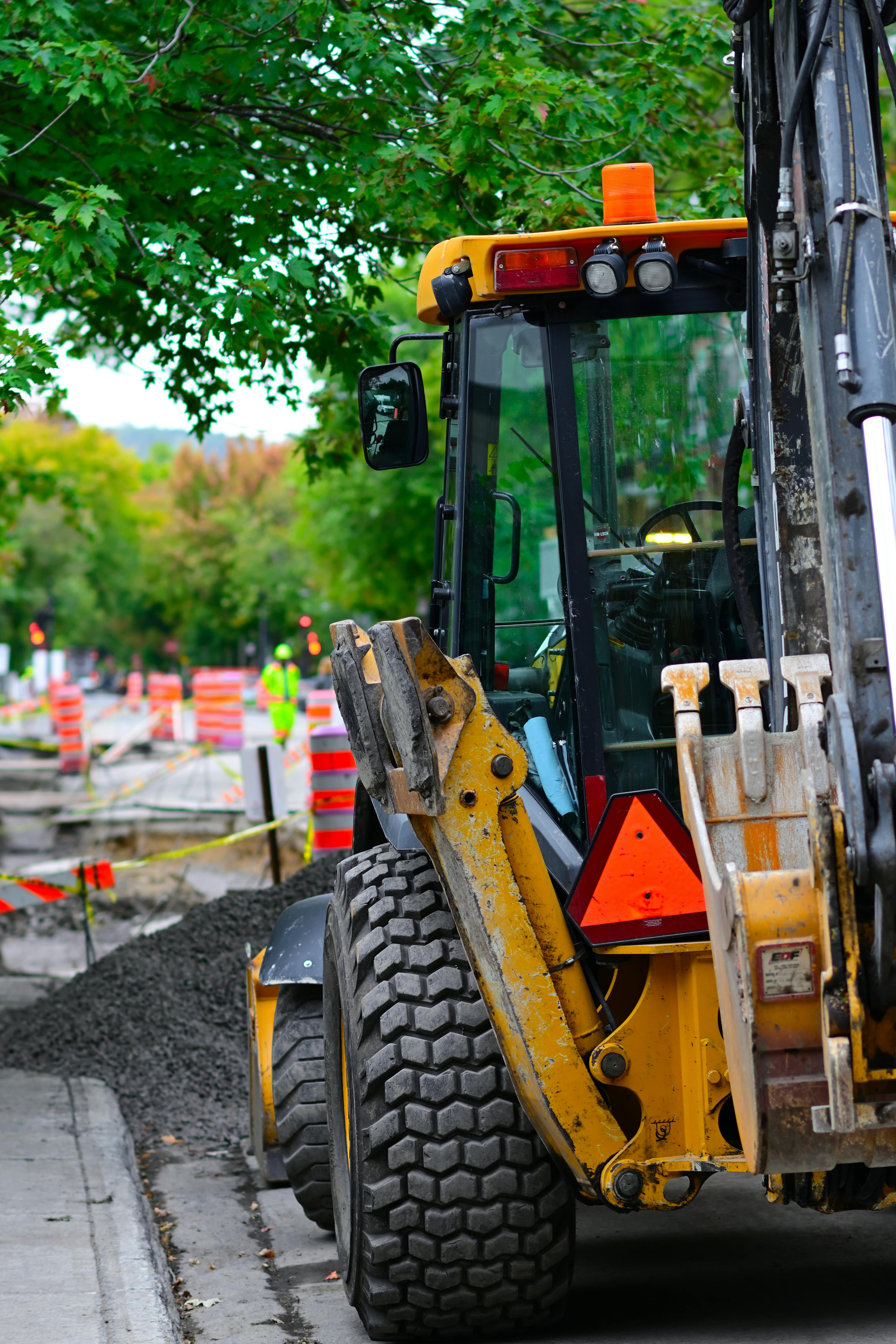Yellow bulldozer working at an outdoor urban construction site with traffic cones and trees.