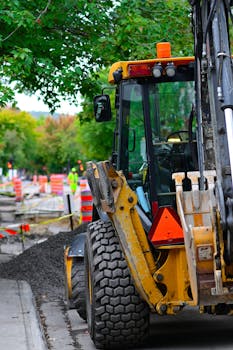 Yellow bulldozer working at an outdoor urban construction site with traffic cones and trees.