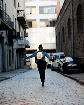 一名背着背包的妇女走在城市的一条鹅卵石小巷里，周围都是建筑物和汽车