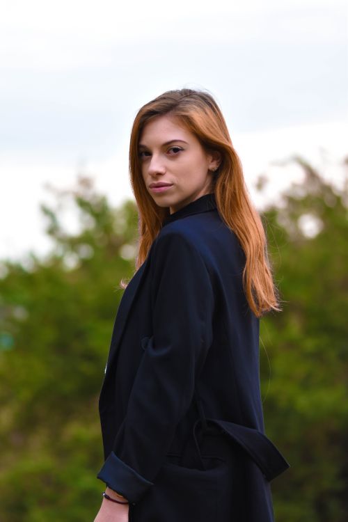 Free A young woman in a black blazer stands confidently against a blurred green background. Stock Photo