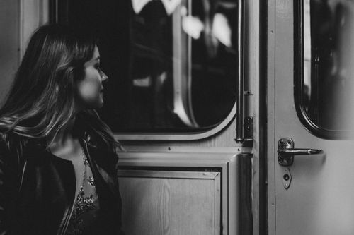 Free A woman in a black jacket gazes thoughtfully out a train window in monochrome. Stock Photo