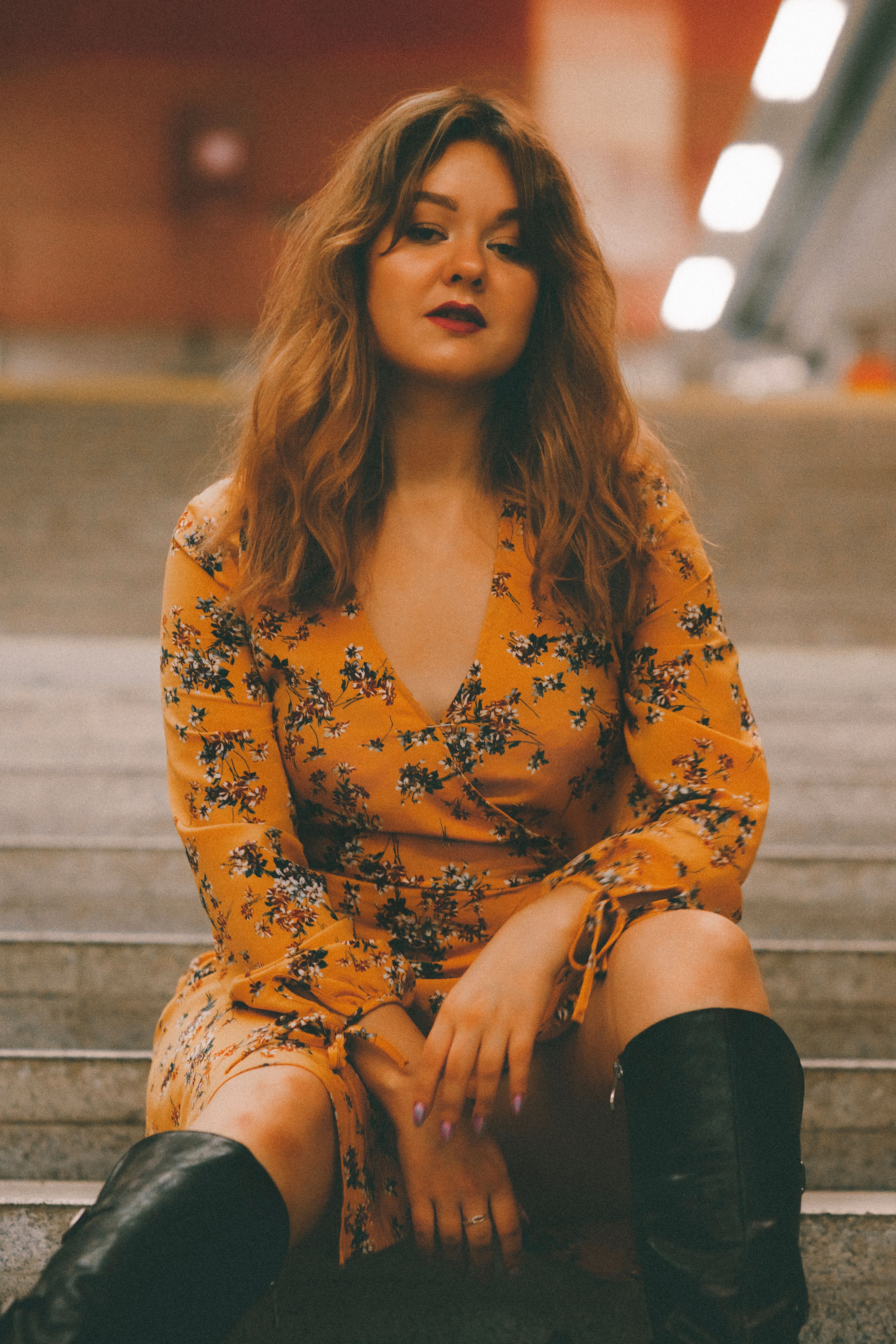 Woman in a floral dress sitting confidently on concrete stairs in an urban setting.