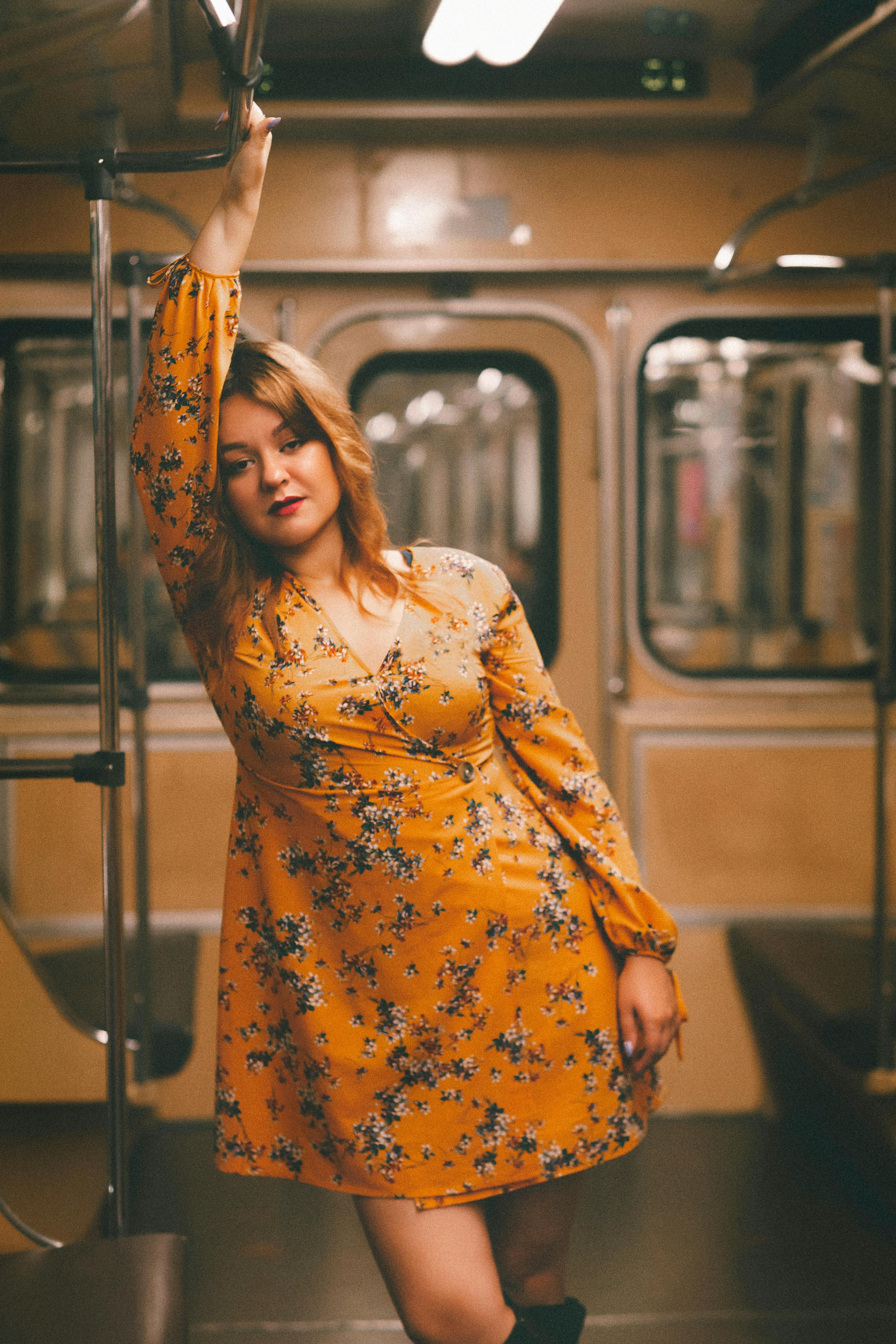 A confident young woman in a floral yellow dress standing inside a metro train.