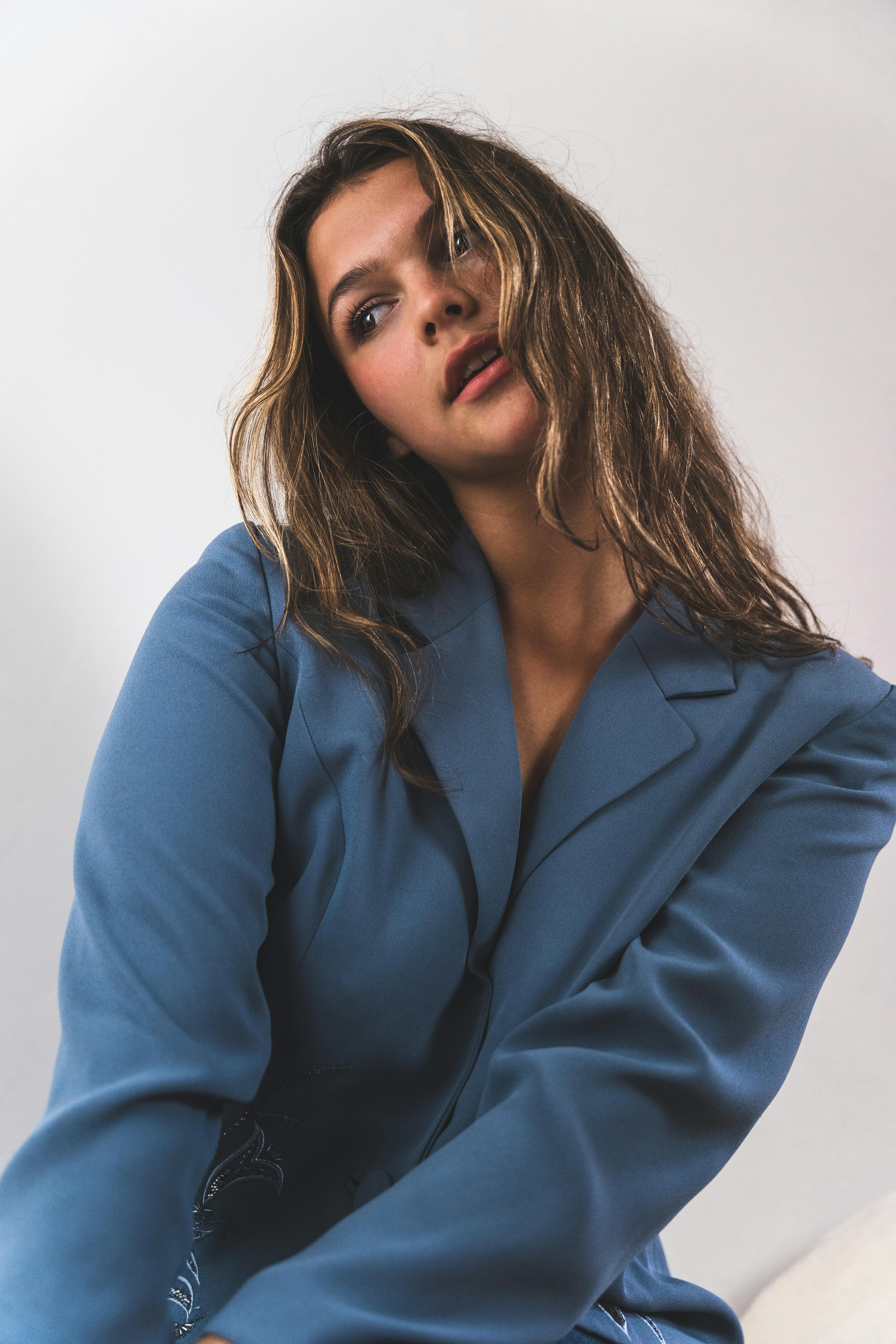 Stylish woman with long hair in a blue blazer posing in a tilted angle studio portrait.