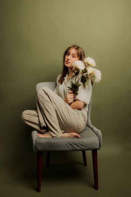 A serene woman sitting on a chair holding white flowers in a studio setting.