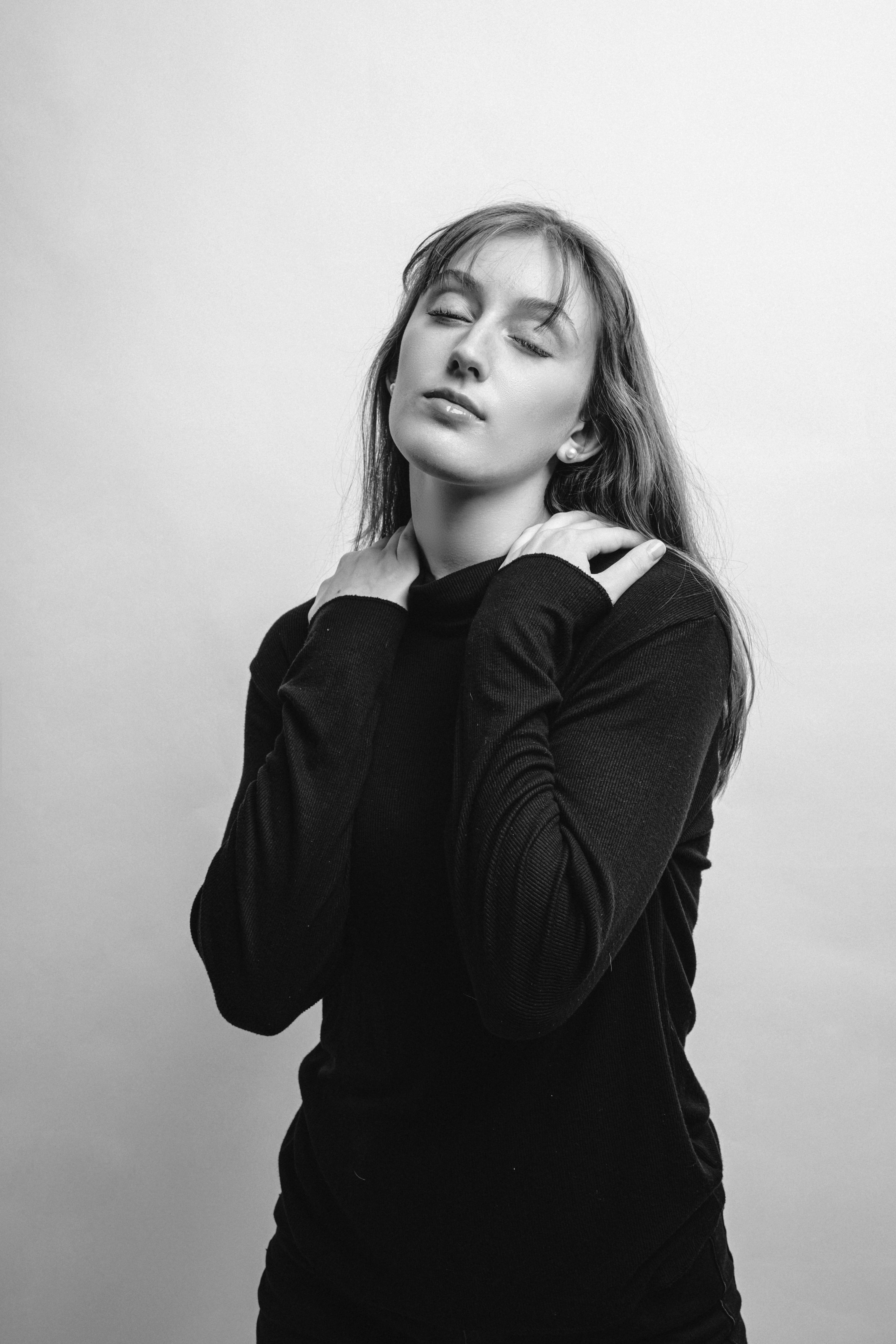 Black and white portrait of a serene woman with closed eyes, hands on shoulders.