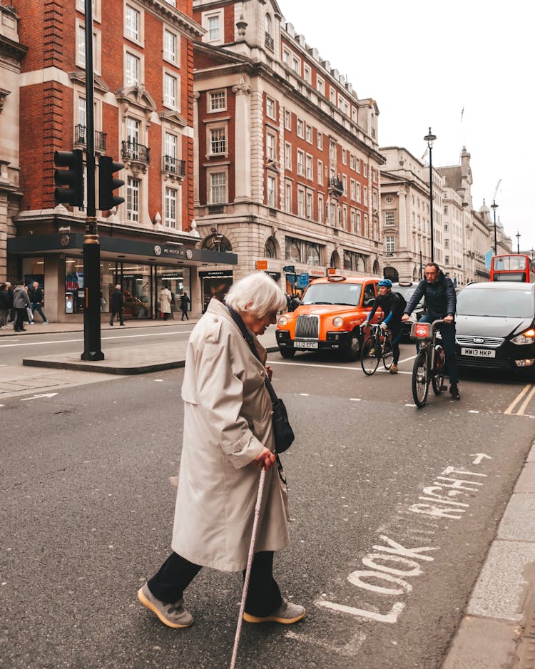 An Elderly Woman With Cane Crossing The Road