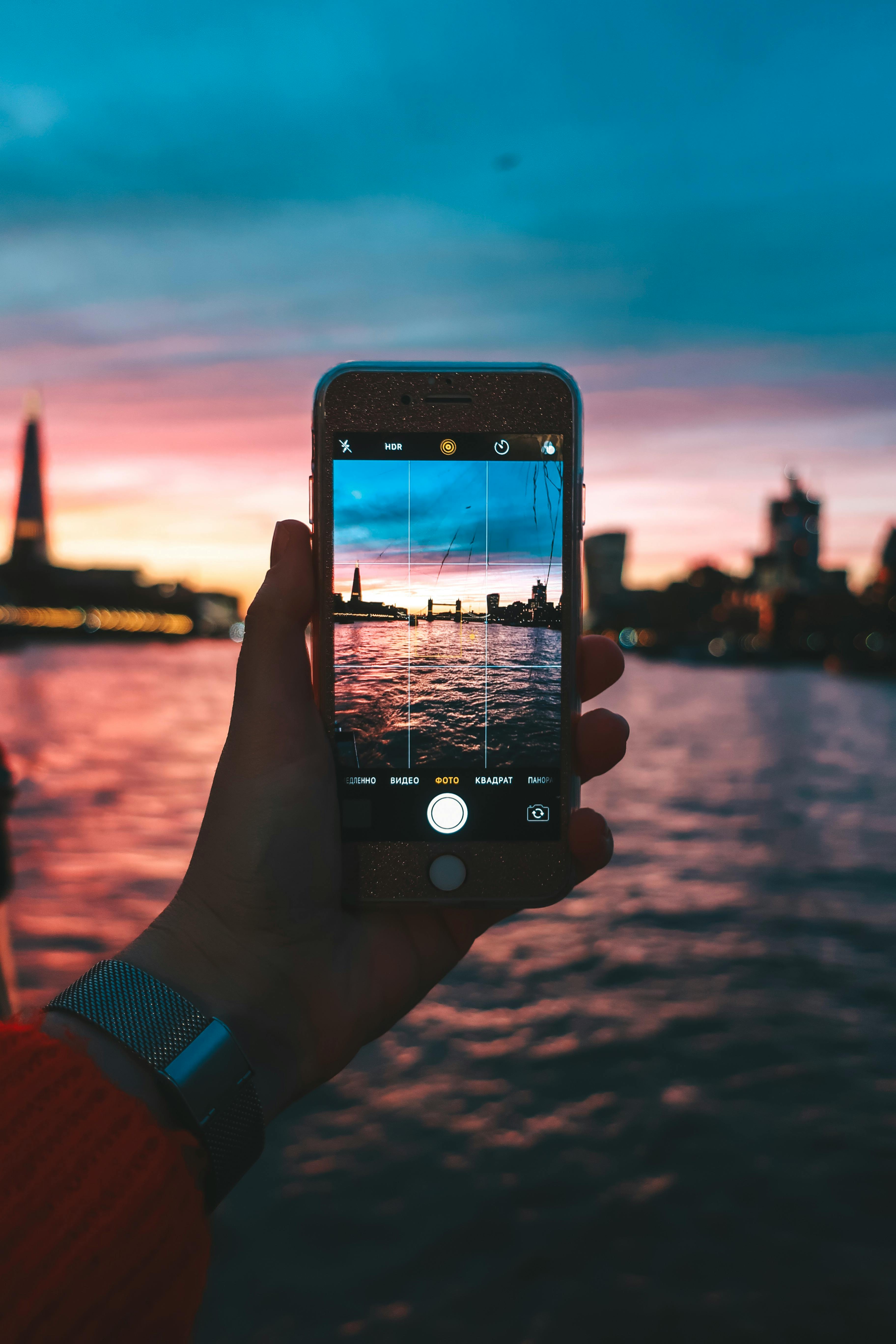 Person photographing a vibrant cityscape at sunset using a smartphone.