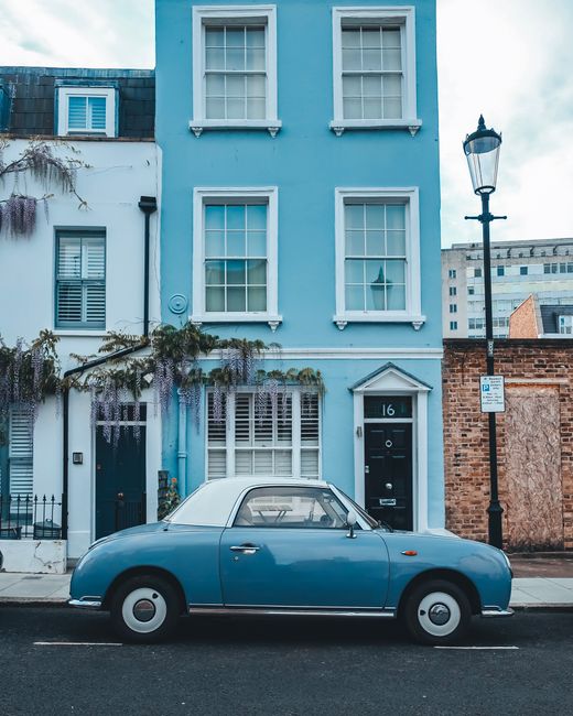 Charming vintage car parked in front of a classic blue townhouse, showcasing urban nostalgia.