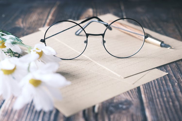 Round Eyeglasses On White Paper Beside Daisies