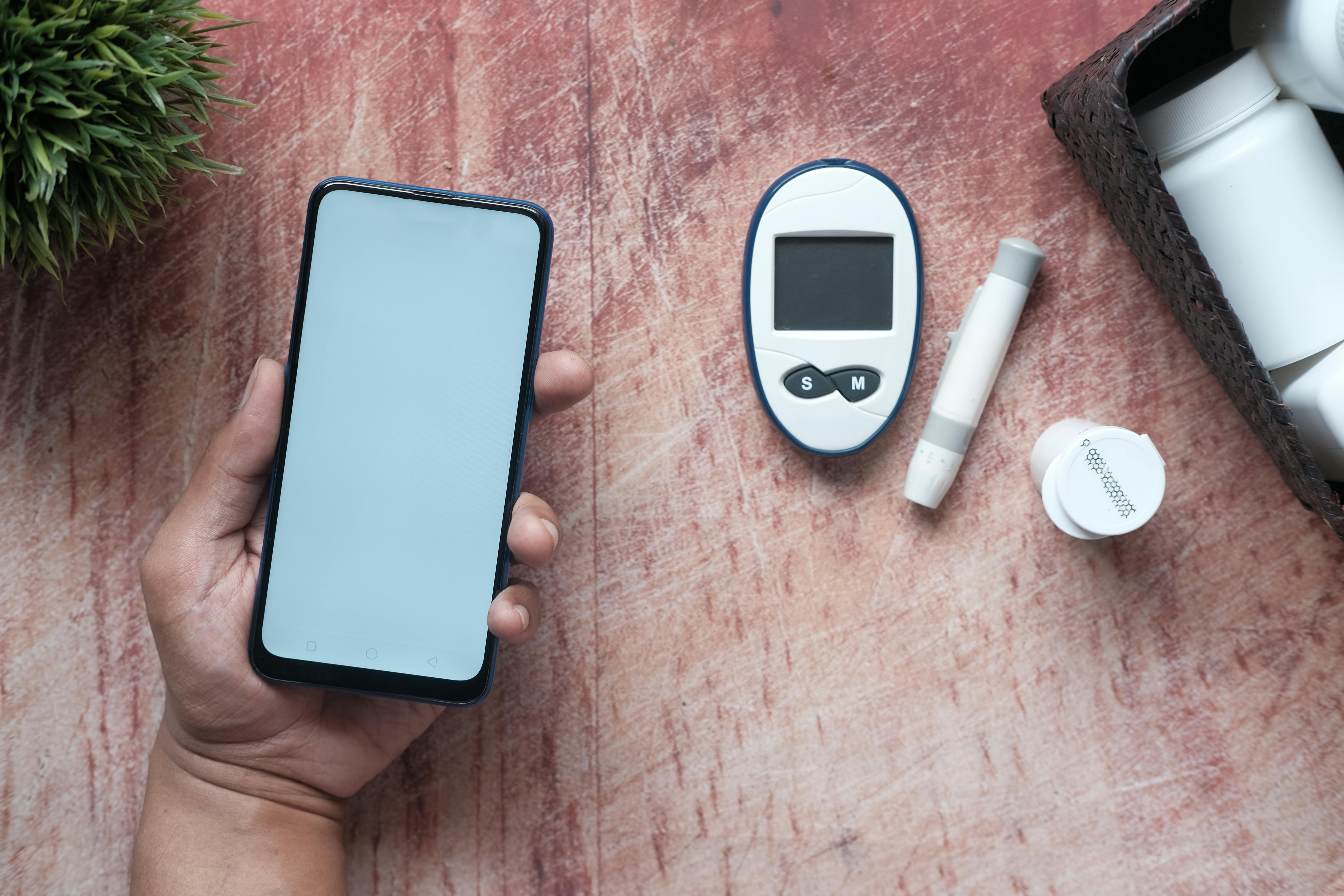 A close-up of a person's hands using a health app on their phone, with medical supplies like a small vial and alcohol swabs on the table beside them