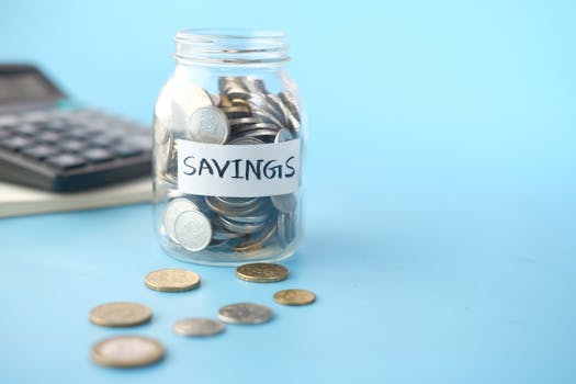 Glass jar labeled 'Savings' filled with coins, beside a calculator on a blue background.