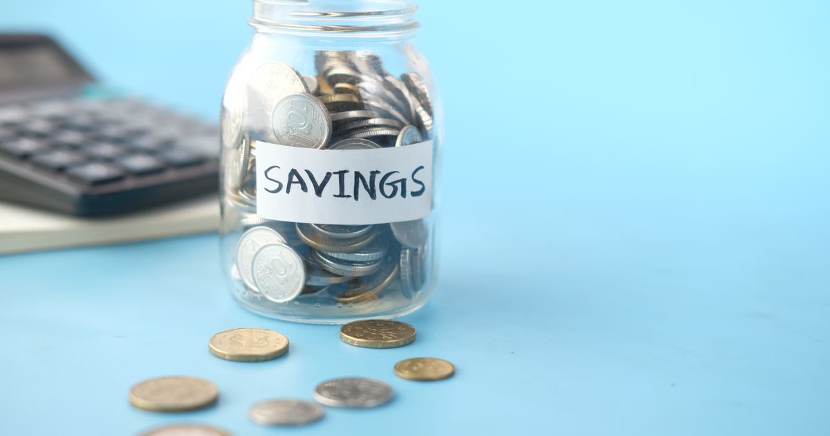 Frasco de vidrio etiquetado como ahorro lleno de monedas junto a una calculadora, para calcular cuánto necesitas en tu fondo de emergencia