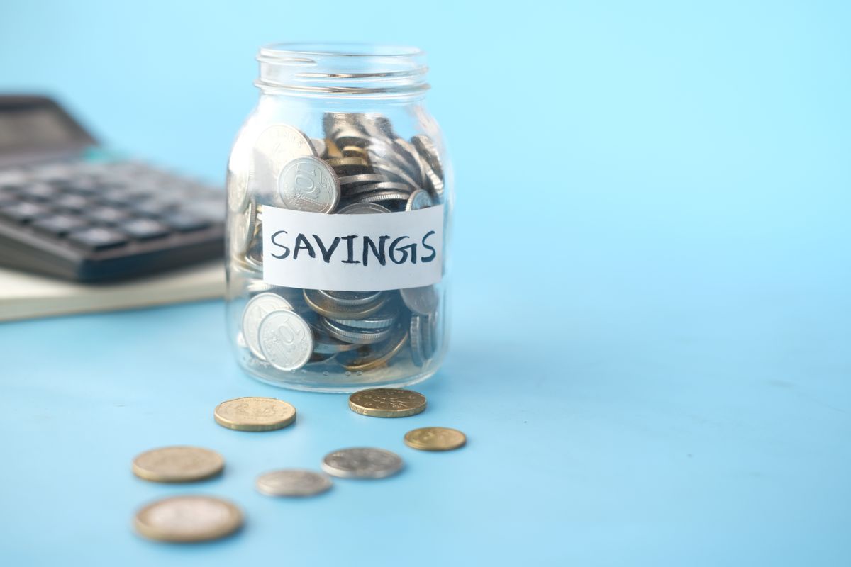 A glass jar labeled savings filled with coins next to a calculator