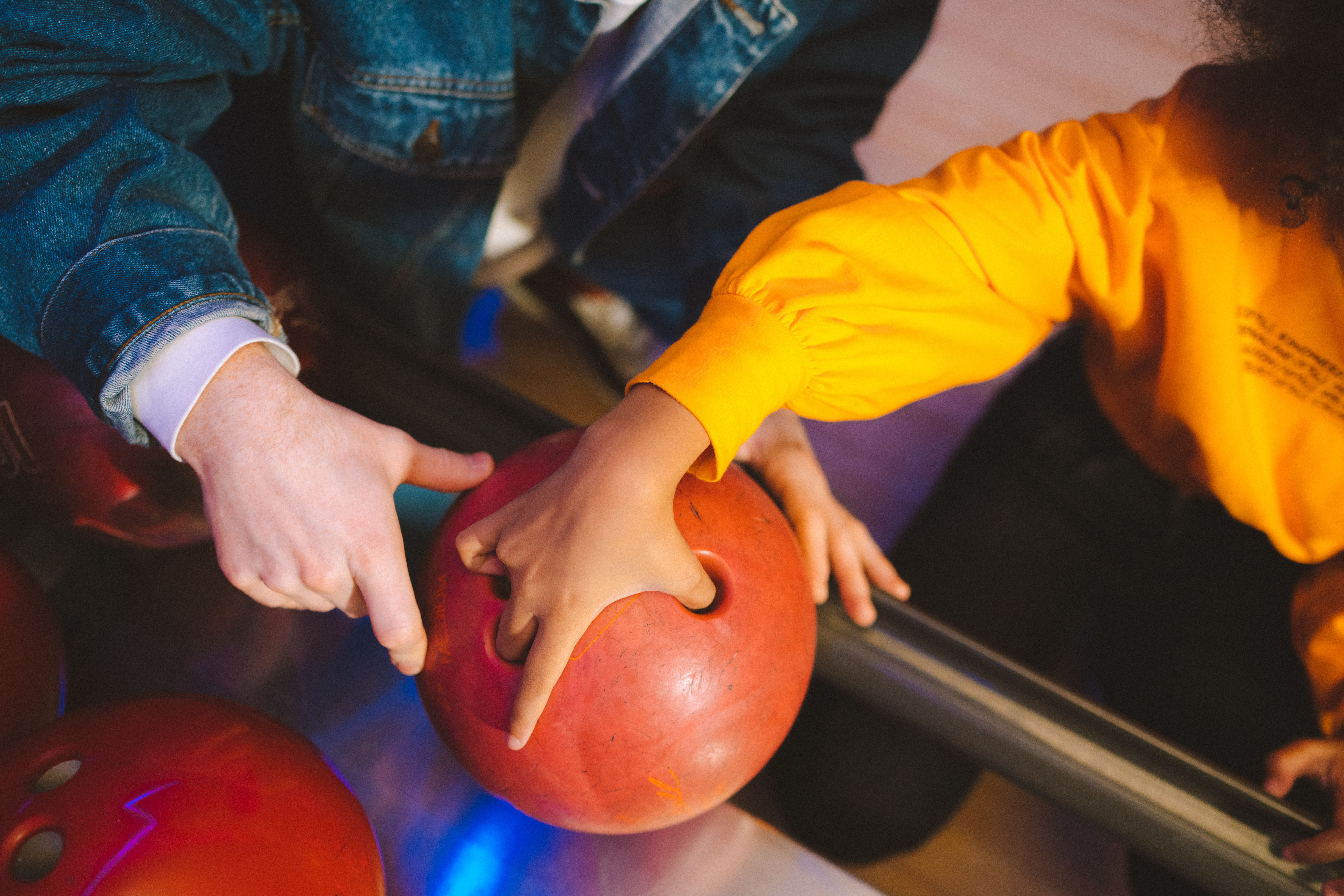 Close-up of hands preparing a red bowling ball in a vibrant bowling alley setting.