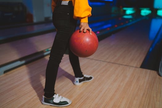 Close-up of a person holding a bowling ball at a bowling alley with vibrant lighting.